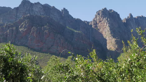 Single-waterfall-falling-in-shade-of-mountain-after-rains,-panning-shot