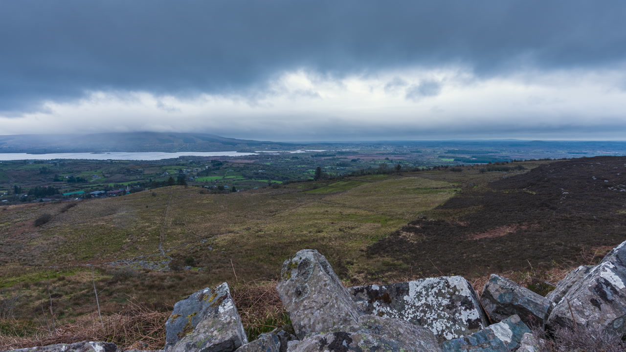 Time lapse of rural landscape with trees in grass and rocky foreground hillside and lake in the distance during an overcast cloudy day in Arigna mountains in county Leitrim in Ireland.