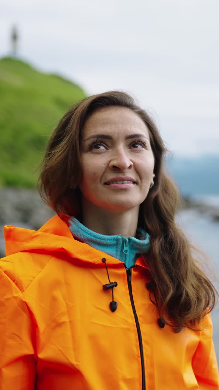 Donna sorridente con giacca arancione su una costa verde