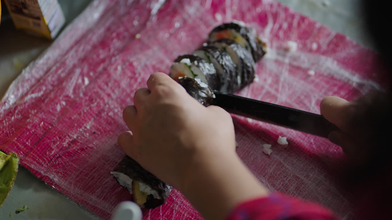 Close-up of hands slicing homemade sushi roll on cutting board, cooking at home