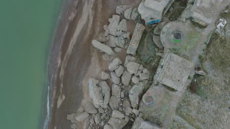 Aerial-birdseye-view-of-abandoned-seaside-fortification-buildings-at-Karosta-Northern-Forts-on-the-beach-of-Baltic-sea-,-waves-splash,-overcast-day,-wide-drone-shot-moving-forward