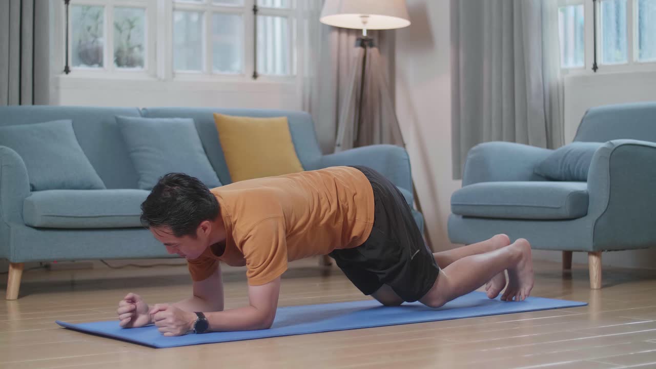 hombre asiático haciendo yoga en el antebrazo en una postura de tabla en la alfombra en casa