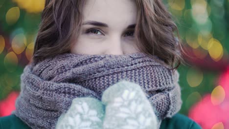 woman wearing scarf and gloves in front of christmas lights