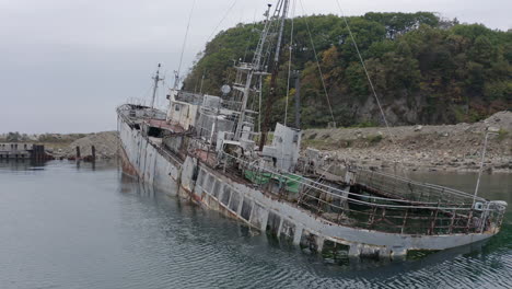 Rusty-grey-half-submerged-shipwreck-anchored-near-the-shore-on-a-cloudy-overcast-day