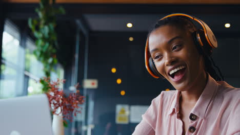 Young-Businesswoman-Wearing-Wireless-Headphones-Making-Video-Call-On-Mobile-Phone-In-Coffee-Shop