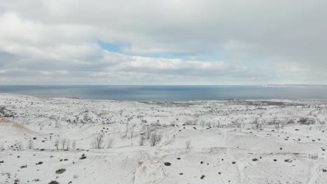 drone flying away from snow covered sand dunes in michigan, usa