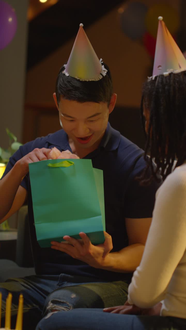 다문화 친구들이 집에서 파티를 열고 남자에게 생일 선물을 주는 수직 비디오