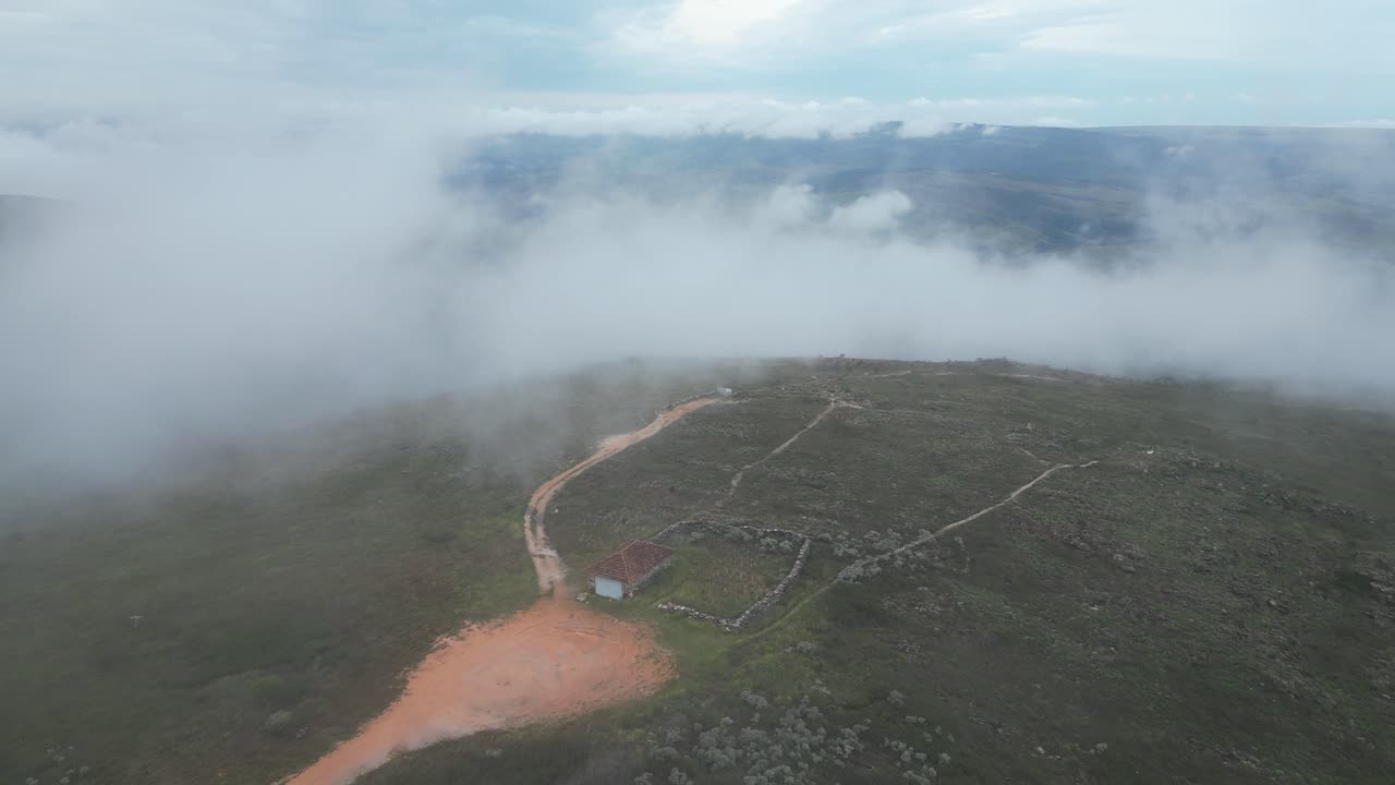 Ascending through cloud, aerial looks onto remote, old stone homestead