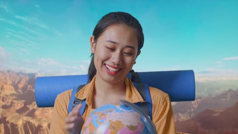 close up of asian female hiker with mountaineering backpack holding world globe in her hands and smiling while traveling at the top of mountain