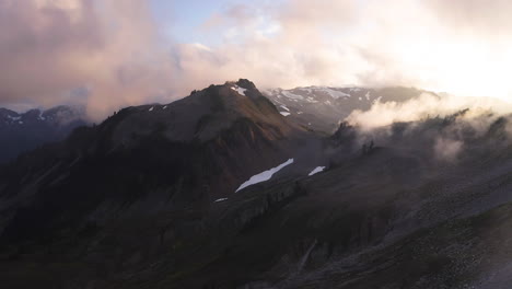 Luz-Amarilla-Dorada-En-El-Cielo-Con-Nubes-Mientras-Los-Picos-De-Las-Montañas-Con-Nieve-Se-Oscurecen-Al-Atardecer