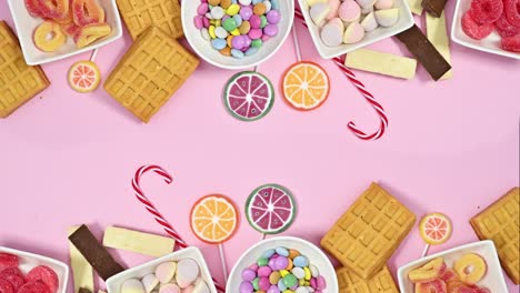 sweet candies decoration appear on top and bottom of pastel pink background. flat lay. stop motion