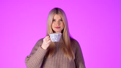 Portrait-Of-Pretty-Blonde-Woman-Drinking-From-Coffee-Mug-And-Looking-At-Camera,-Studio-Shot-With-Pink-Background