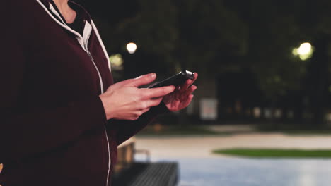 sportive curly girl using mobile phone to activate bluetooth headphones and then start to run in the park at night