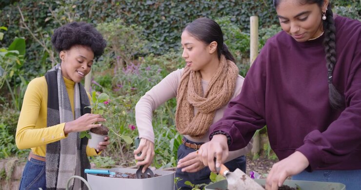 African American friends scooping potting soil, planting seedlings at backyard table for garden