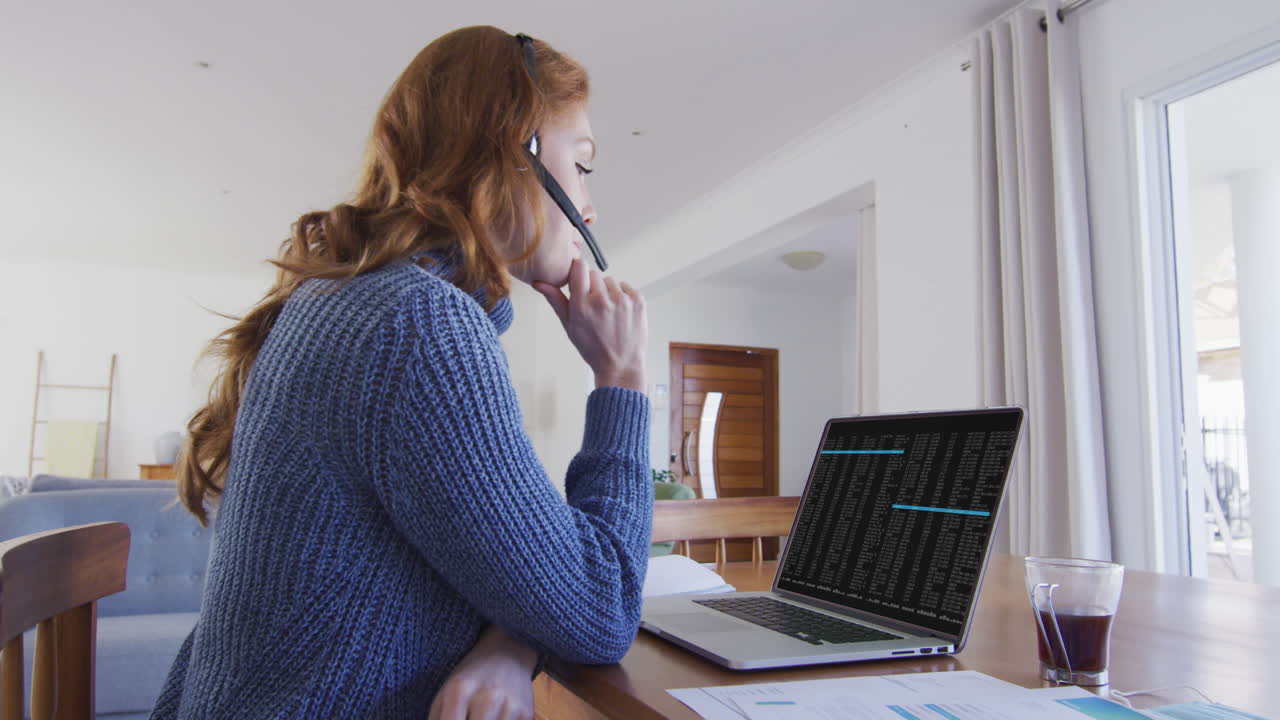Kaukasisk kvinde sidder ved skrivebord og ser på kodning og databehandling på laptopskærmen.