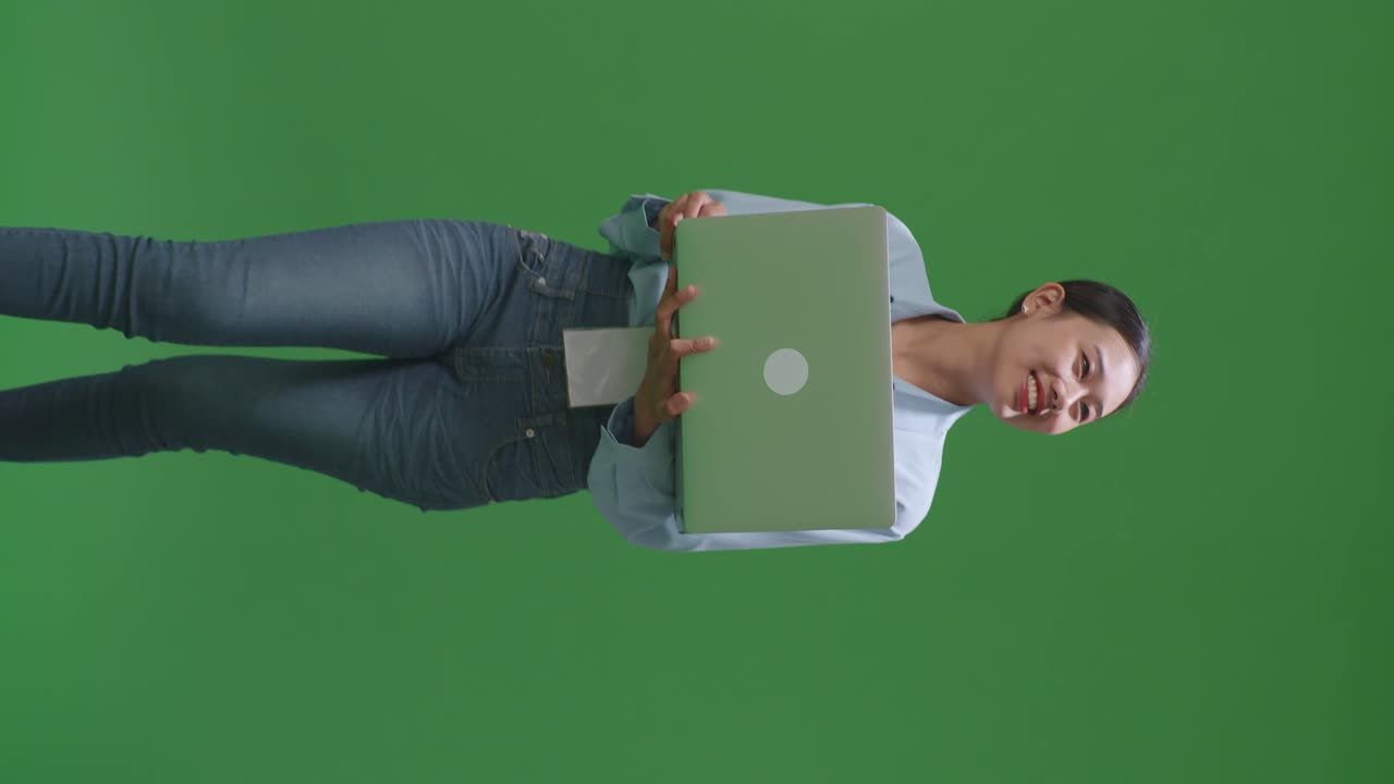 mujer de negocios asiática usando una computadora portátil mientras camina en el fondo de la pantalla verde en el estudio