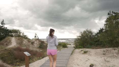 young woman goes on wooden path to beach near the sea