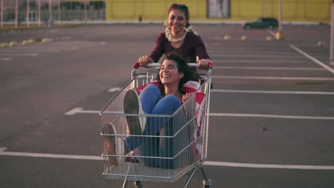 fashion funny young hipster teen girls having fun at the shopping mall parking, riding in shopping cart holding the american flag