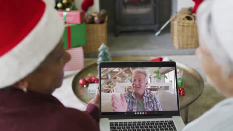 diversas amigas mayores usando una computadora portátil para una videollamada de navidad con un hombre feliz en la pantalla