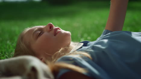 smiling blonde girl lying blanket on green field holding hand up close up.