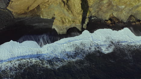 foamy waves breaks through coastal mountains at black sand beach of reynisfjara in southern iceland