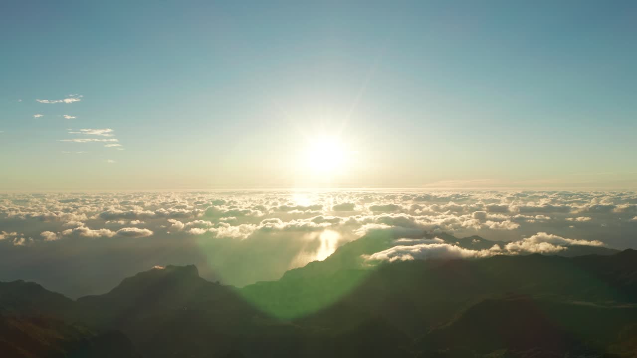 Heavenly bright sunrise above clouds with lens flare and mountains below, aerial
