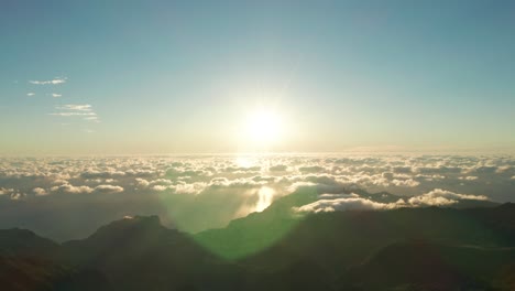 heavenly bright sunrise above clouds with lens flare and mountains below, aerial