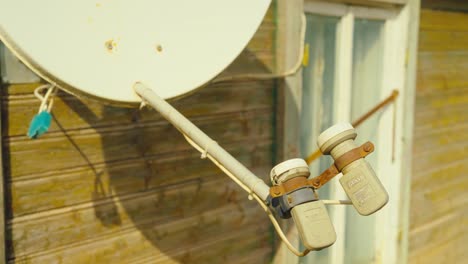 detailed view of a satellite dish with dual receivers fixed on a rustic wooden house under warm sunlight. location: daugavpils, latvia (daugavpils, latvija)