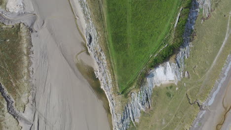 Aerial-top-down-view-of-the-shoreline-around-a-grassy-hill-at-low-tide,-on-bright-sunny-day