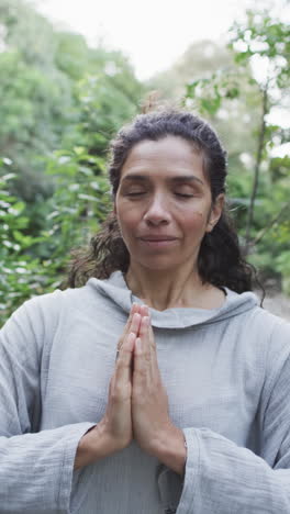 vertical video of focused biracial woman practicing yoga in sunny garden, slow motion