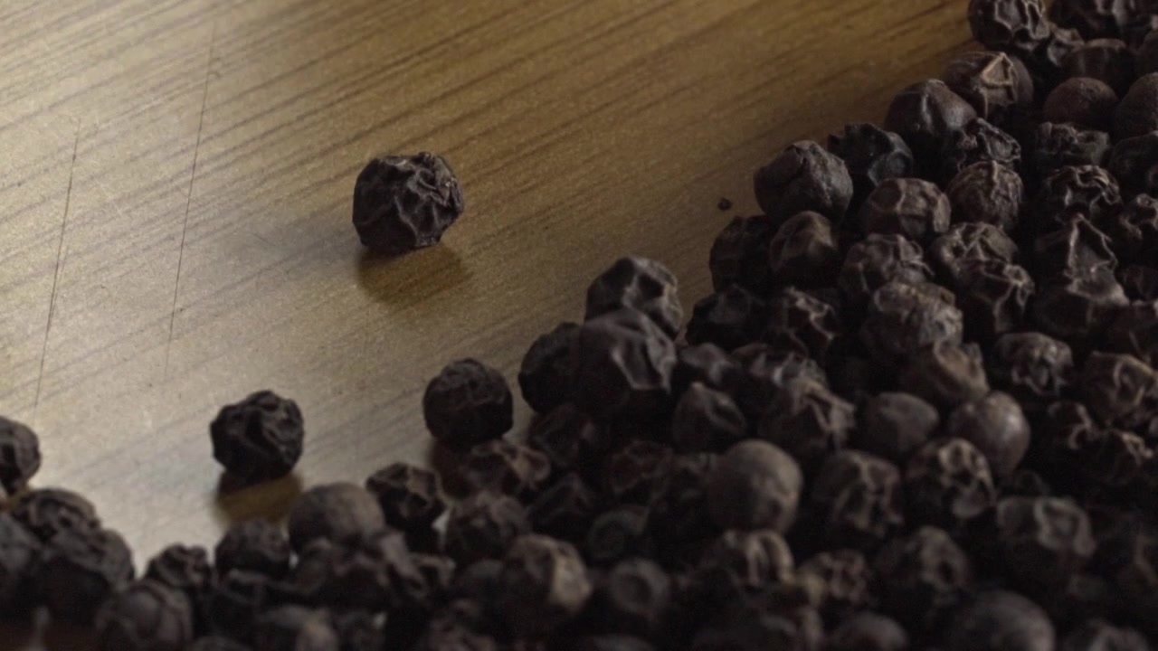 Makrovisning av svarte pepperkorn som flyttes med stoff over en treoverflate, fremhever krydderhåndtering, naturlig tekstur og tilberedning av kulinariske ingredienser.