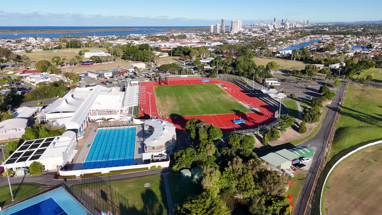 Drone footage captures a vibrant sports park with fields, tracks, and pools on a sunny day in Gold Coast, Australia