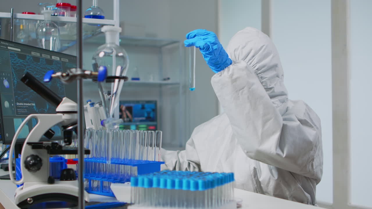 Lab technician in coverall examining samples of liquid