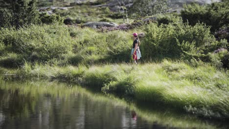 a woman with a small white terrier on the grassy bank of the shallow lake