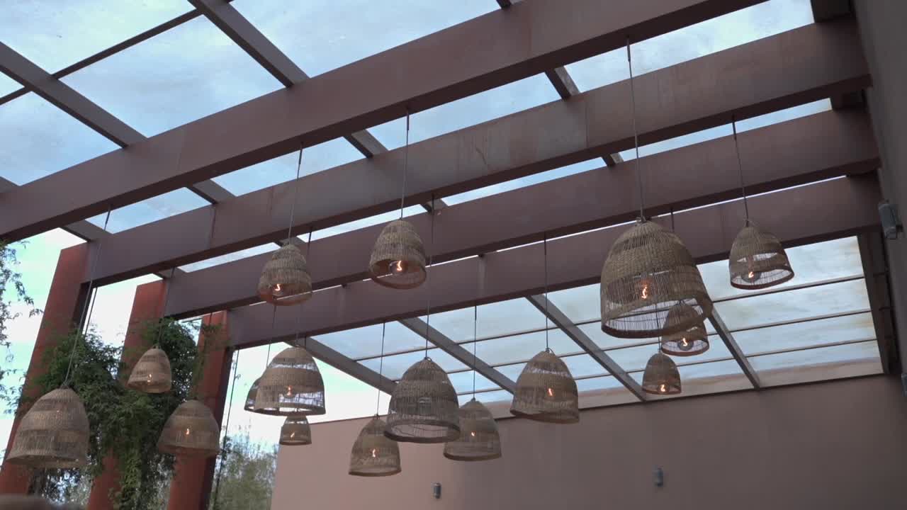 Stylish wicker lamps suspended under a modern pergola with a glass ceiling, creating a cozy ambiance