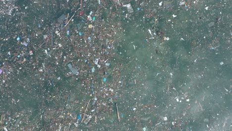 baja altitud de arriba hacia abajo panorámica drone tiro de agua contaminada llena de basura flotando sobre arrecife de coral muerto en las aguas tropicales turquesa de bali indonesia