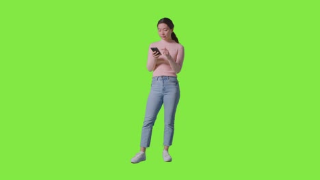 Full-length-Studio-Shot-Of-Woman-Checking-Mobile-Phone-And-Getting-Good-News-Message-Against-Green-Screen