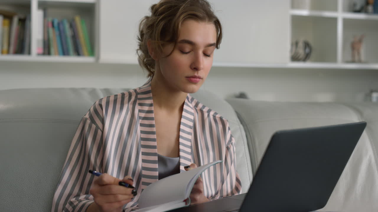 Millennial student making notes working on laptop computer at home closeup.