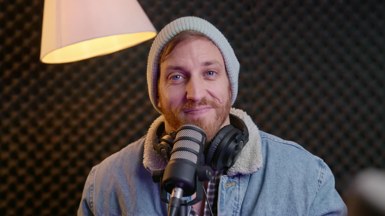 hipster podcaster looks directly at camera, smiling and nodding while wearing headphones on neck. Confidence, connection, and professionalism podcasting, content creation, communication, modern media