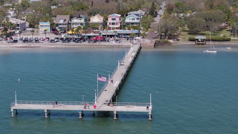 drone flying in a semi circle around a dock in a coastal town setting with people walking and cars