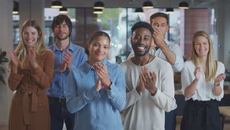 Portrait-Of-Applauding-Multi-Cultural-Business-Team-Standing-In-Modern-Open-Plan-Office