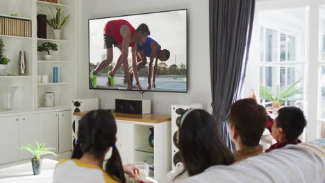 Composite-of-happy-family-sitting-at-home-together-watching-athletics-running-on-tv