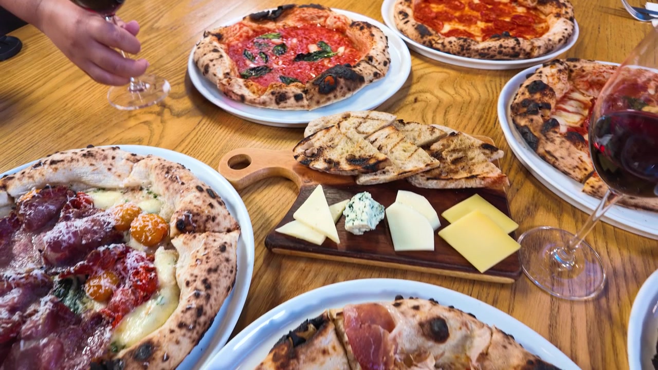 Draufsicht auf verschiedene Pizzen, eine Käseplatte und Rotwein während eines Restaurantbesuchs.