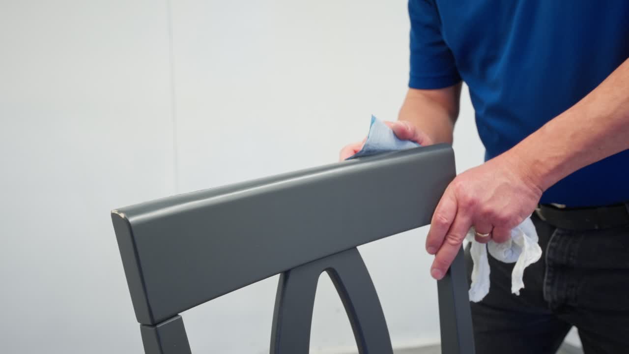Close up captures man sanding grey dining chair back with sandpaper indoors