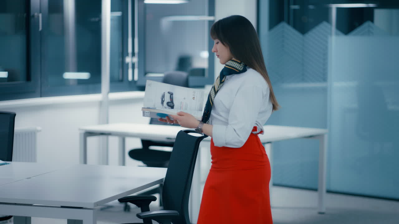 Alta dirigente sfoglia le pagine di una rivista di design in un ufficio, indossando una gonna rossa e una camicia bianca