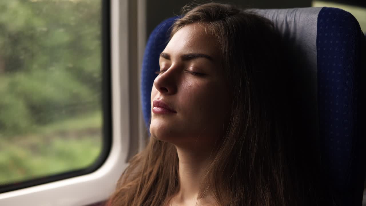 Aim footage of a gorgeous young woman travelling by train. Have a nap. Closed eyes. Sitting near the window. Long haired brunette