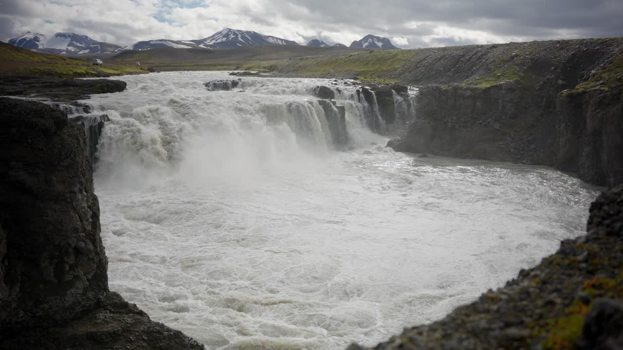 fotografía estática de cascadas gloriosamente épicas y un río con montañas cubiertas de nieve en el fondo