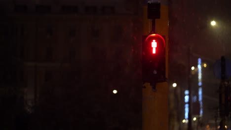 snow falls around red led do not walk sign at night in front of building