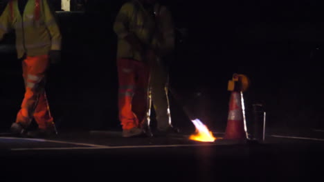 vista en cámara lenta de un trabajador de la carretera usando una lanza térmica para quemar líneas blancas de una carretera principal antes de volver a pintar por la noche