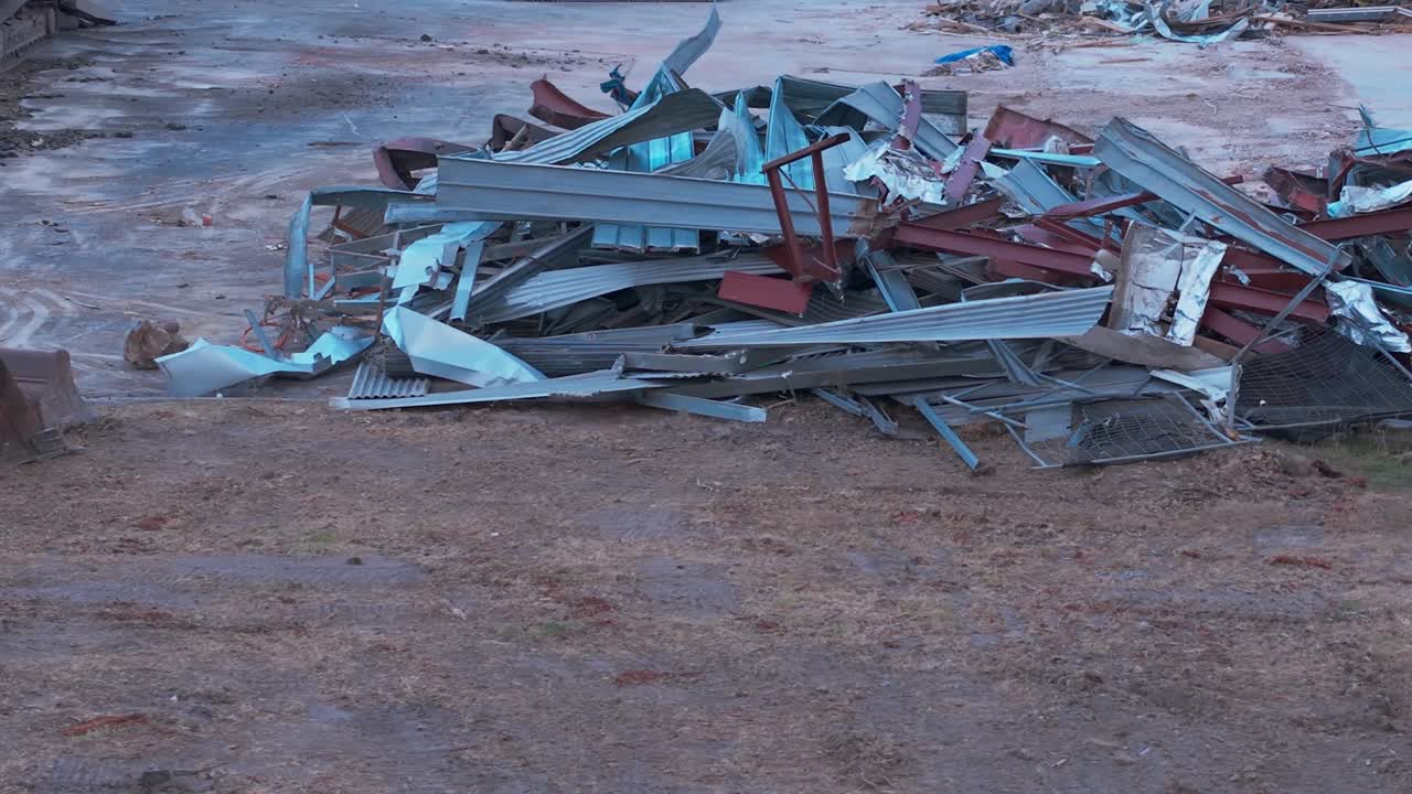 Uma grande pilha de vigas de metal e destroços em um canteiro de obras vazio em Melbourne, capturada em iluminação suave. O local está desprovido de pessoas, destacando o lixo industrial com uma foto estática.